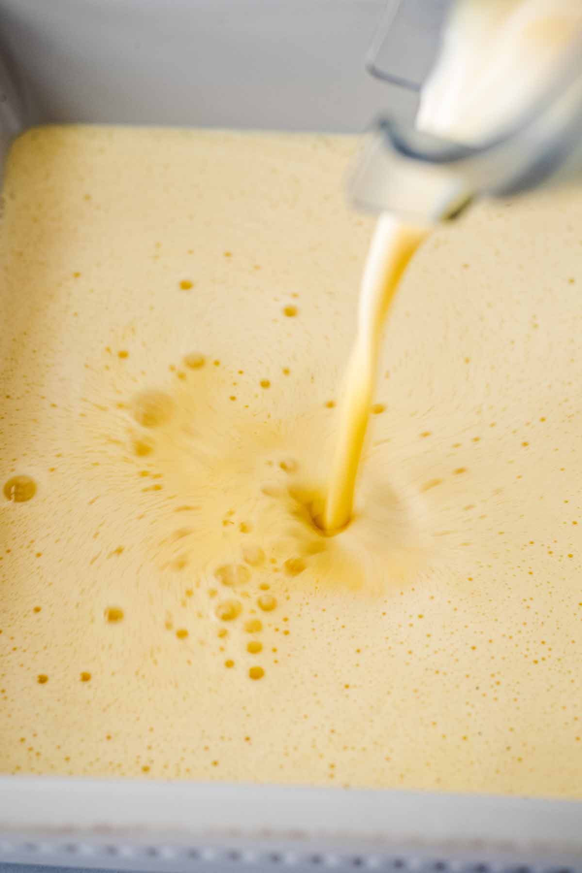 Blended ingredients being poured into a shallow baking dish.