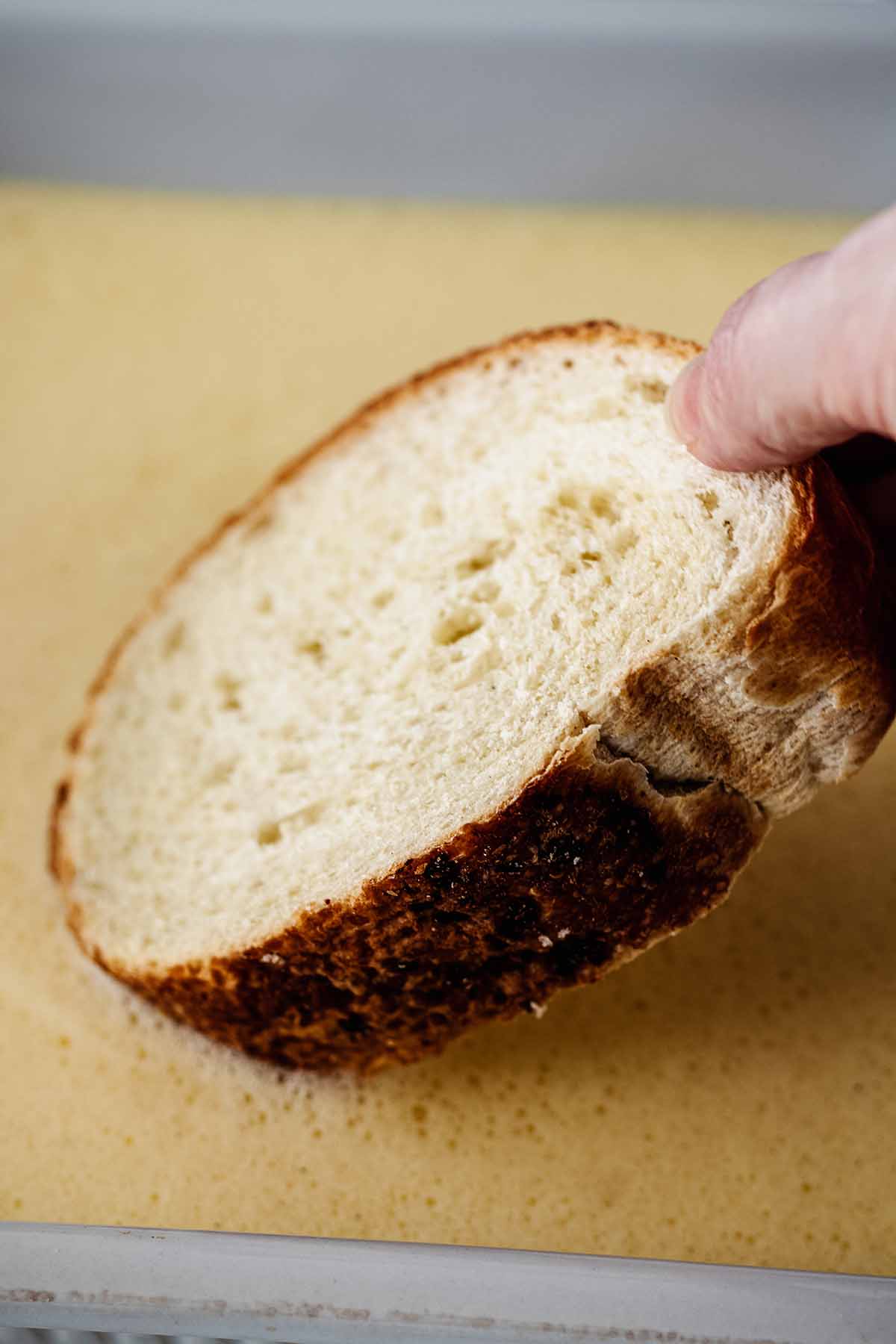 Slice of bread being dipped into egg and milk mixture.