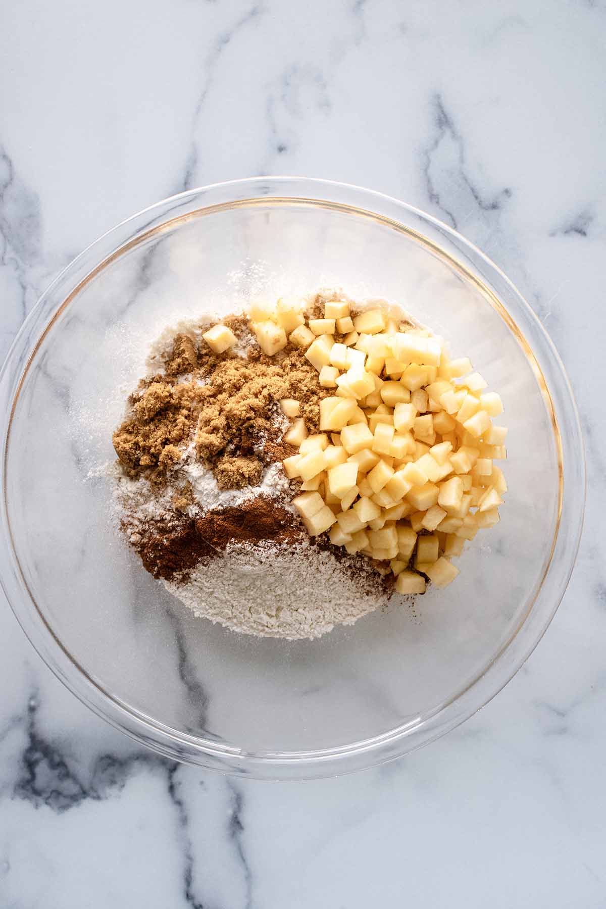 Top view of dry ingredients and apple cubes in a large glass bowl