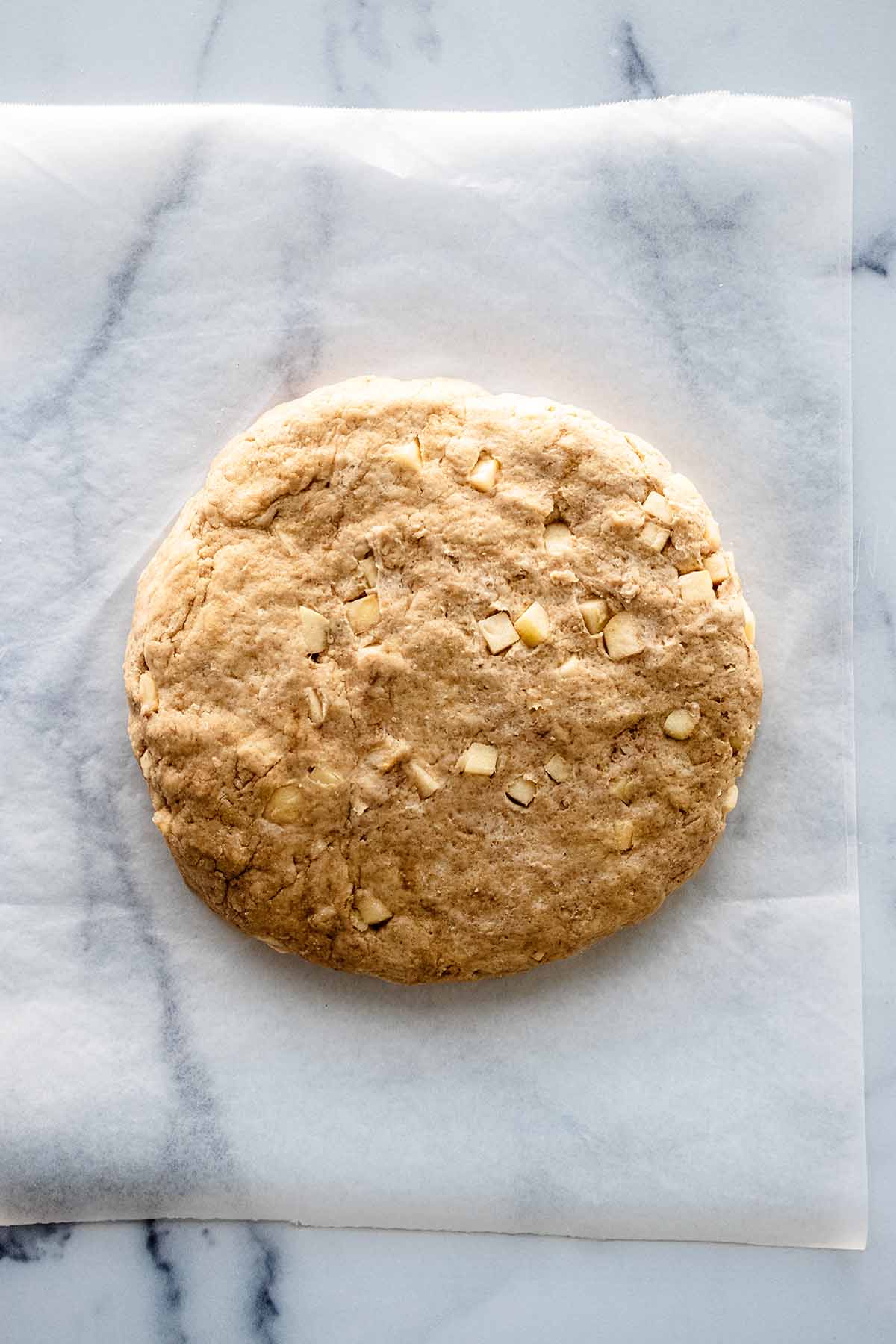 Top view of a disc of apple scones dough on a piece of wax paper