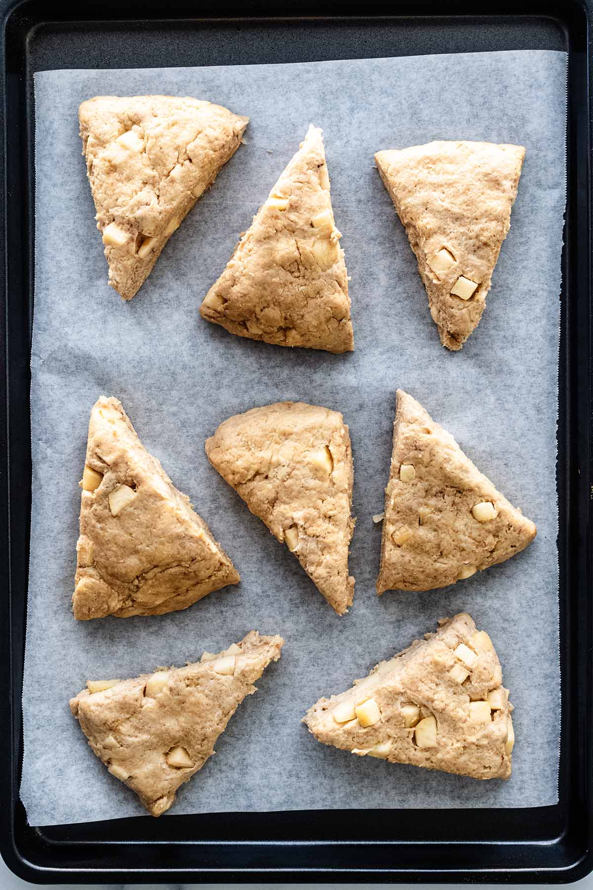 Top view of unbaked apple scones on parchment paper and baking pan