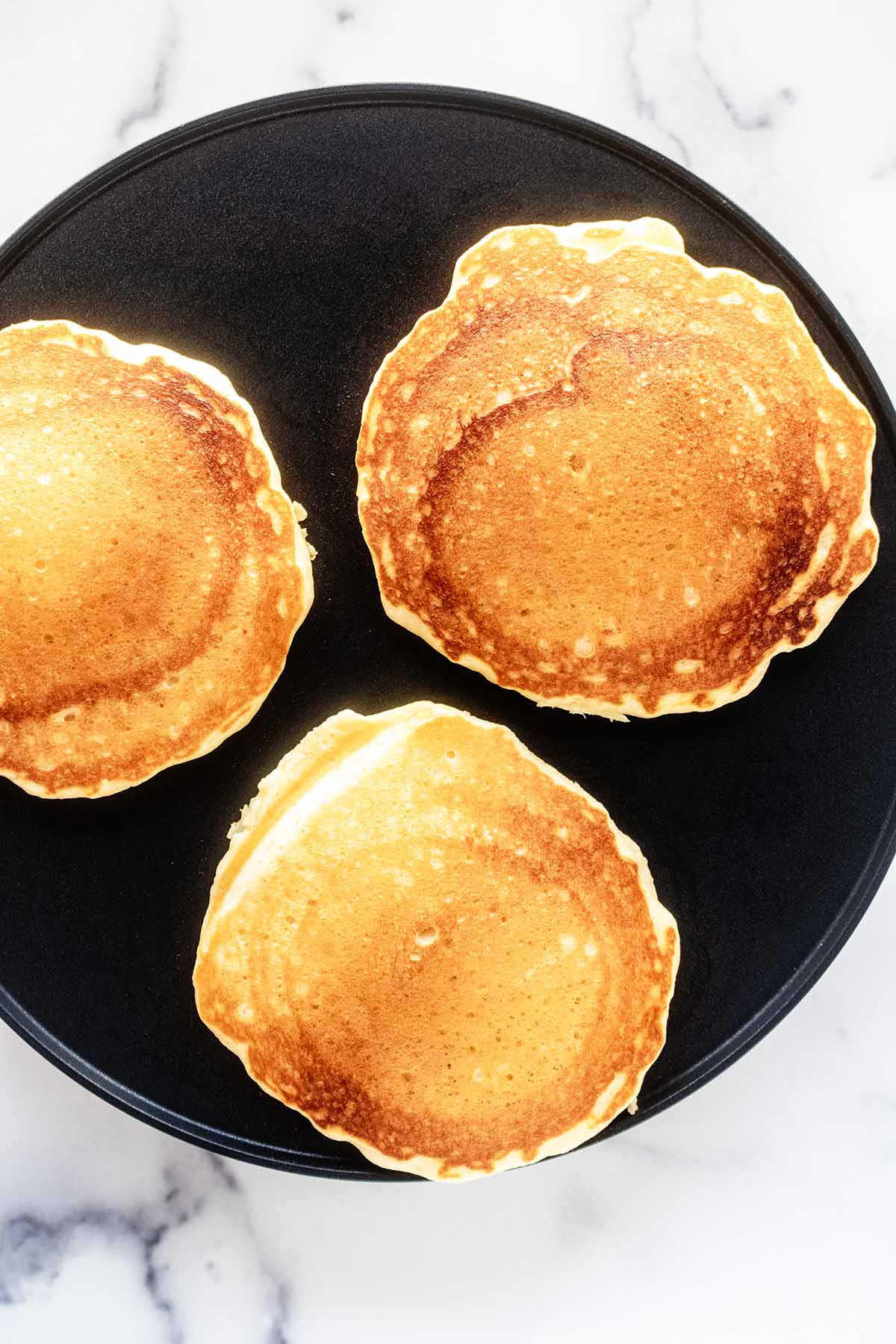 Overhead view of golden pancakes cooking on a griddle