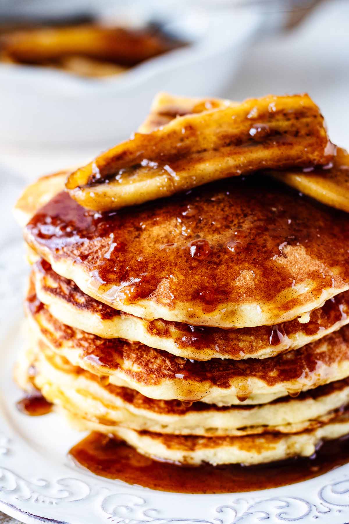 Close up of a stack of bananas Foster pancakes on a white plate with a gold fork