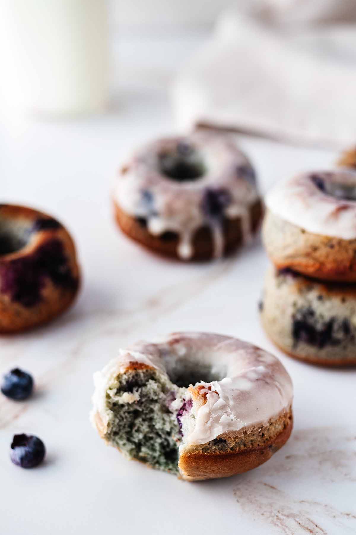 Blueberry donuts and blueberries on a marble surface. One donut has a bite taken out.