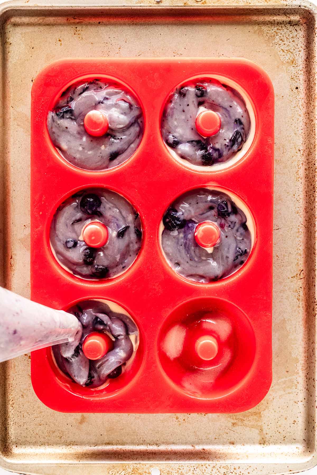 Blueberry donut batter being piped into donut pan