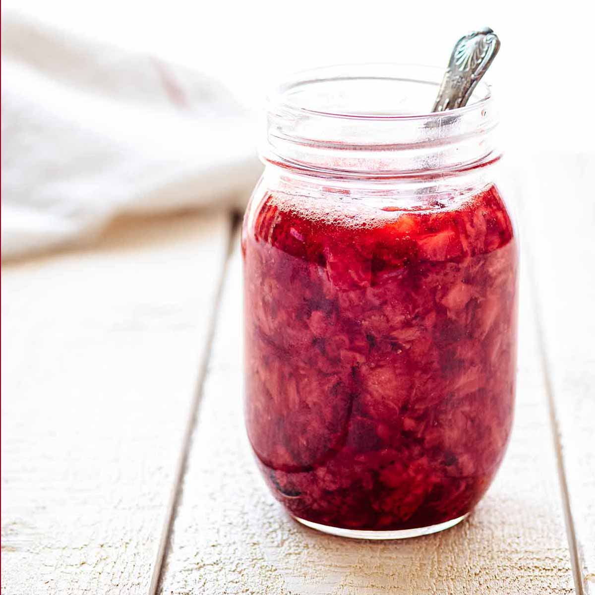 Close up of a jar of strawberry compote with a spoon