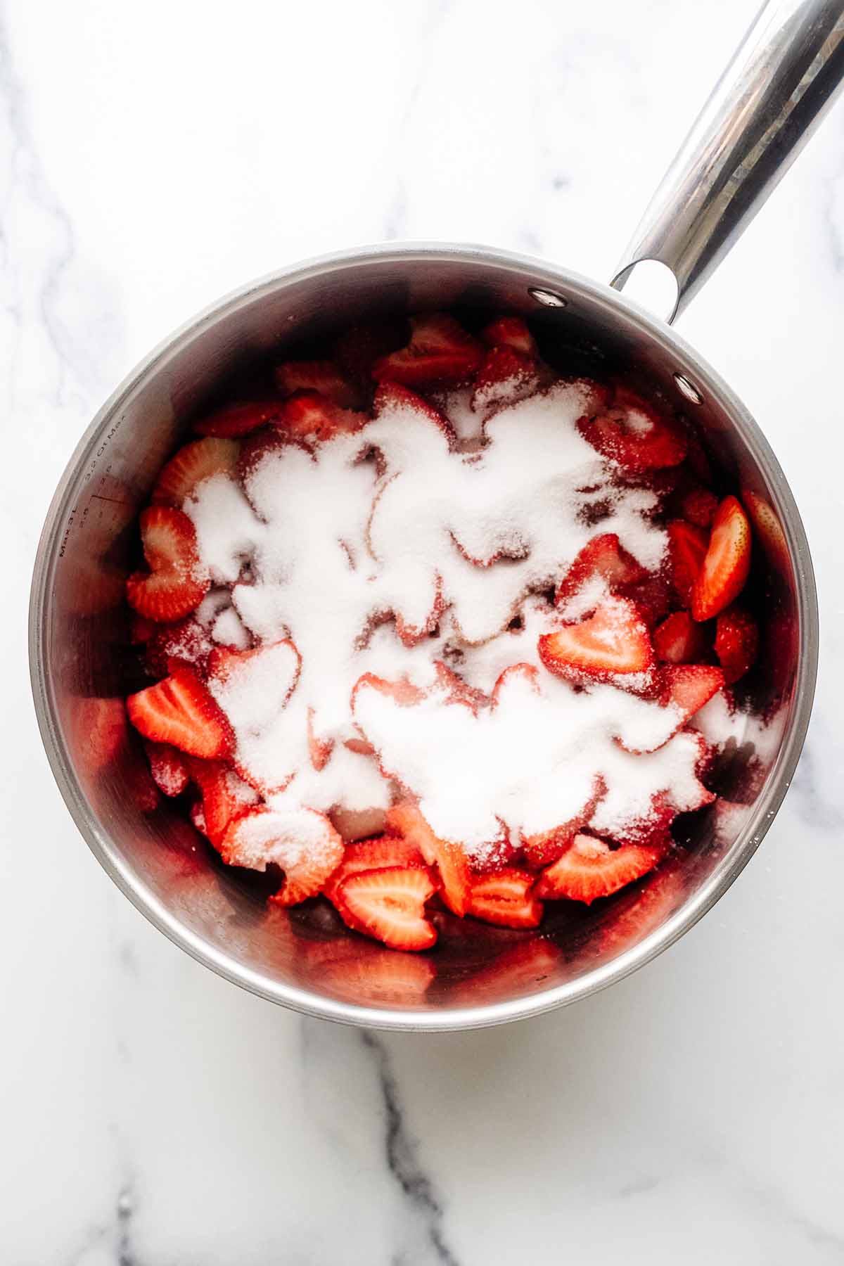 Overhead view of strawberry compote ingredients in a stainless steel saucepan