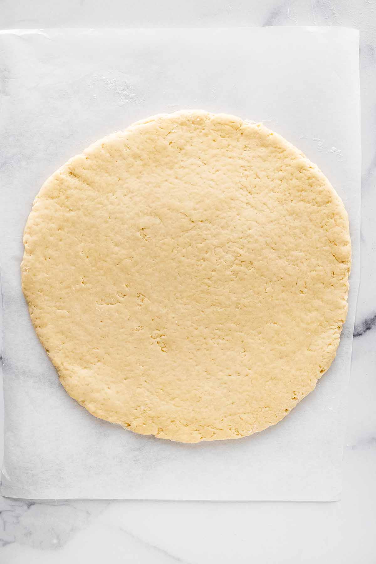 Overhead view of rolled out scone dough on a piece of wax paper on a marble surface.