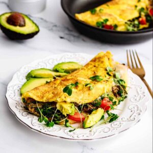 Loaded California omelette on a white plate with sliced avocado and a gold fork