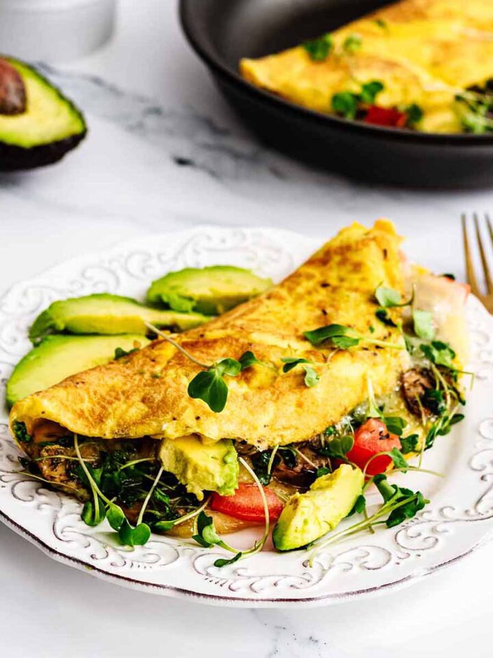 Loaded California omelette on a white plate with sliced avocado and a gold fork