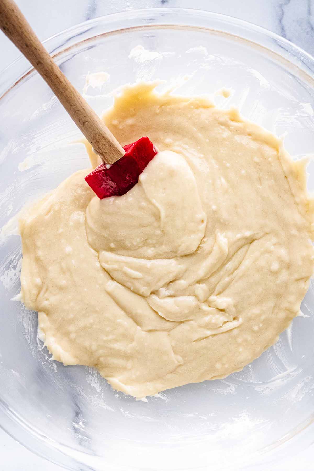 Overhead view of muffin batter in a large glass bowl with a red rubber spatula