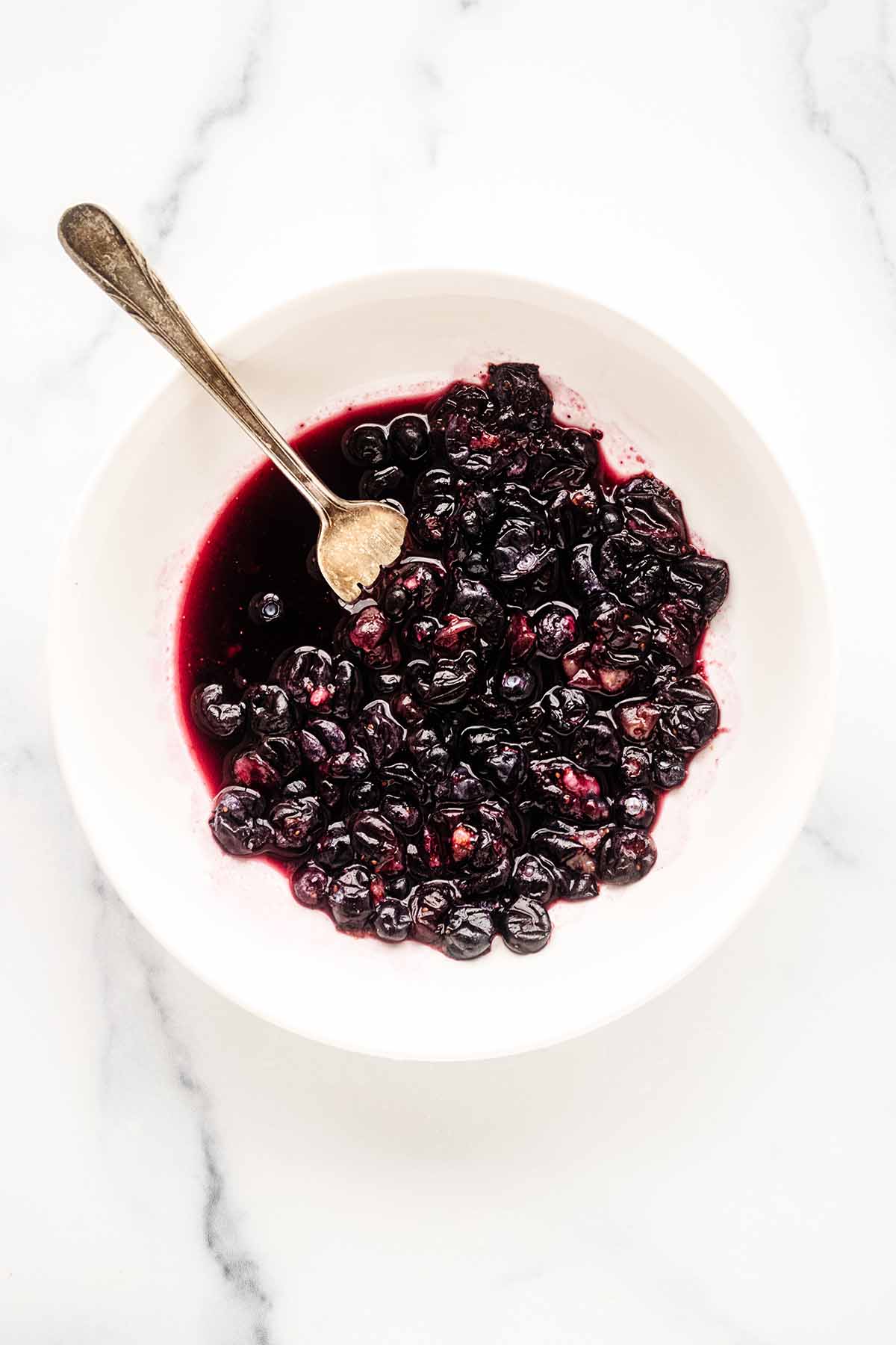 Overhead view of blueberries being crushed with a fork in a white bowl