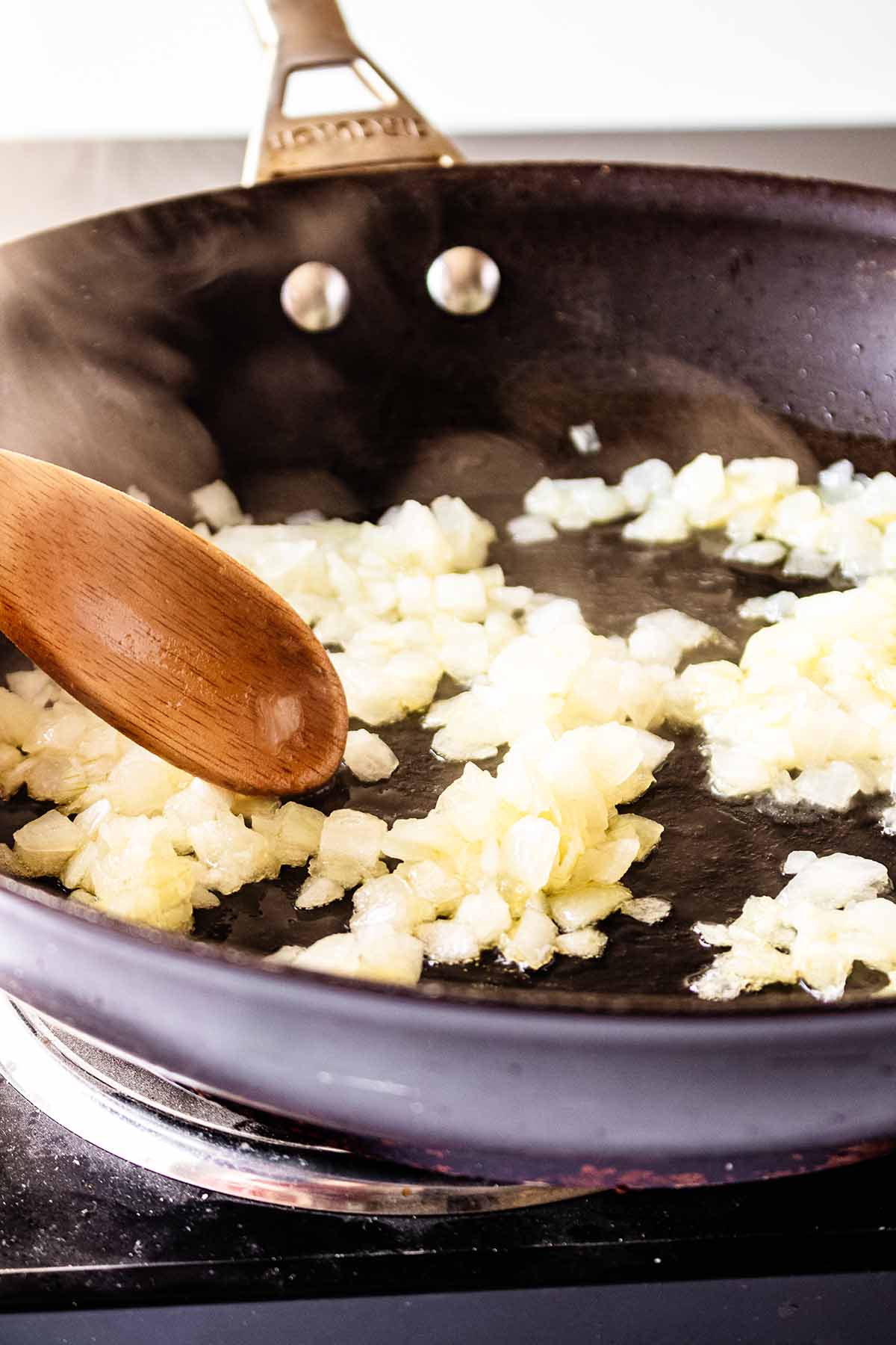 Chopped onion cooking in a skillet with a wooden spoon.