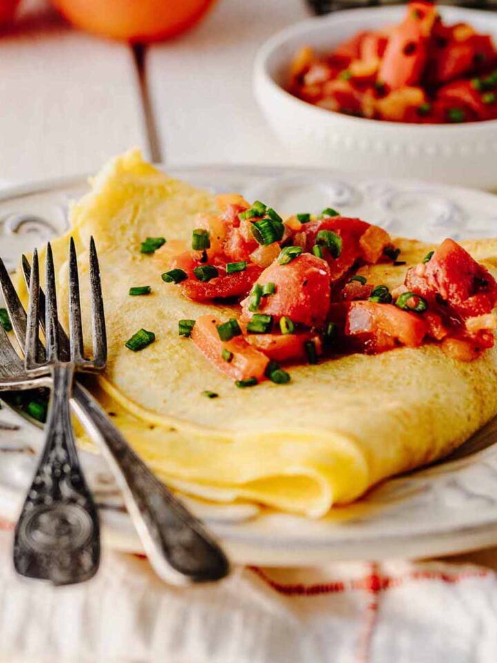 Folded omelette topped with tomato topping on a white plate with two forks