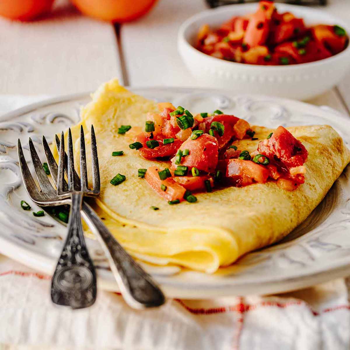 Folded omelette topped with tomato topping on a white plate with two forks