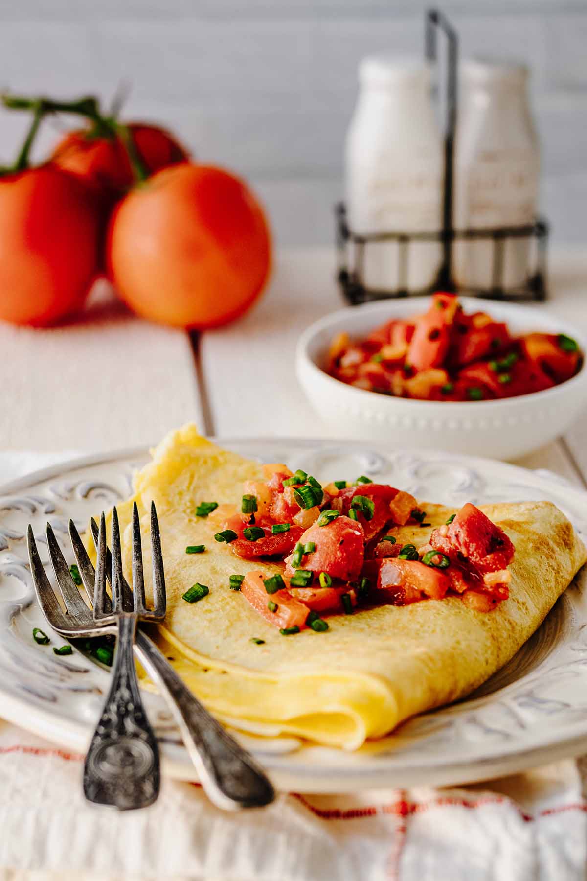 Folded tomato omelette covered with tomato topping and chopped green onion on a white plate with two forks.