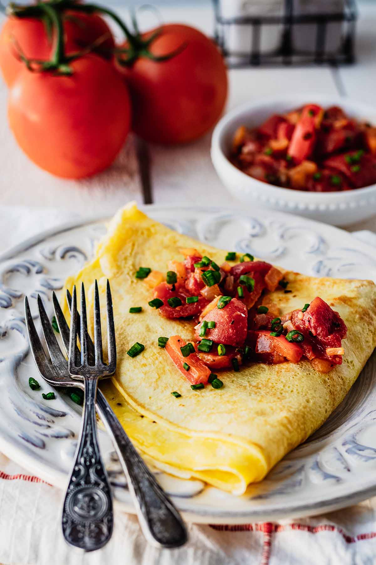 Folded omelette covered with tomato topping sitting on a white plate with two forks.