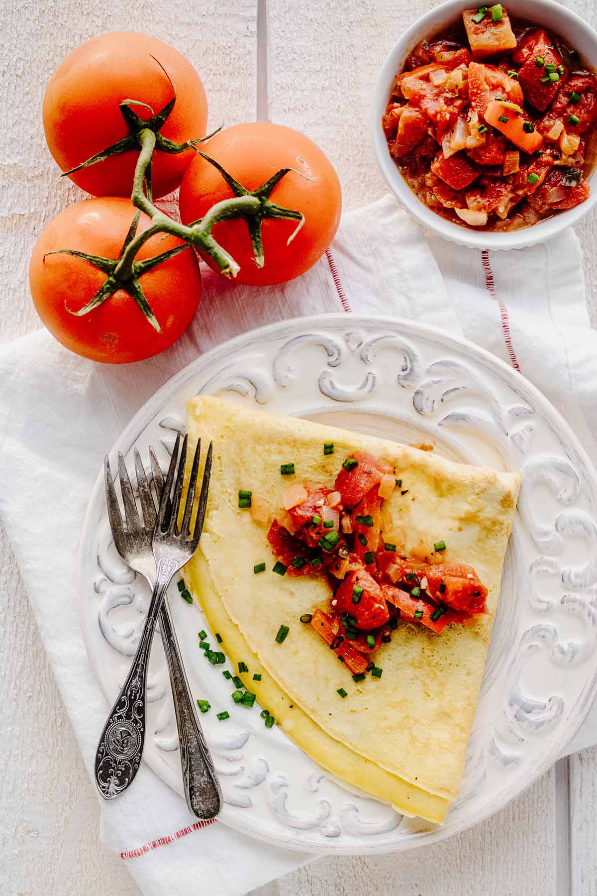 Overhead view of folded cheesy omelette covered with tomato topping on a white plate with two forks.