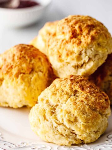Stack of four air fryer biscuits on a white plate with a small bowl of strawberry jam.