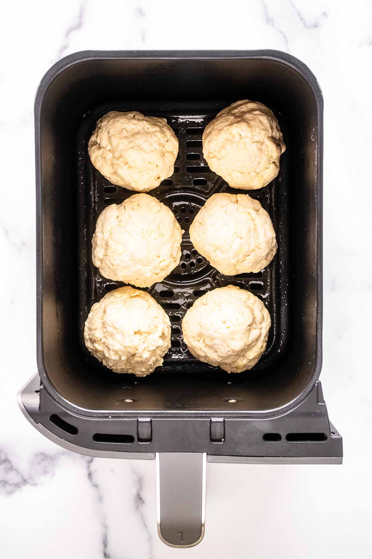 Six unbaked biscuits in an air fryer basket.