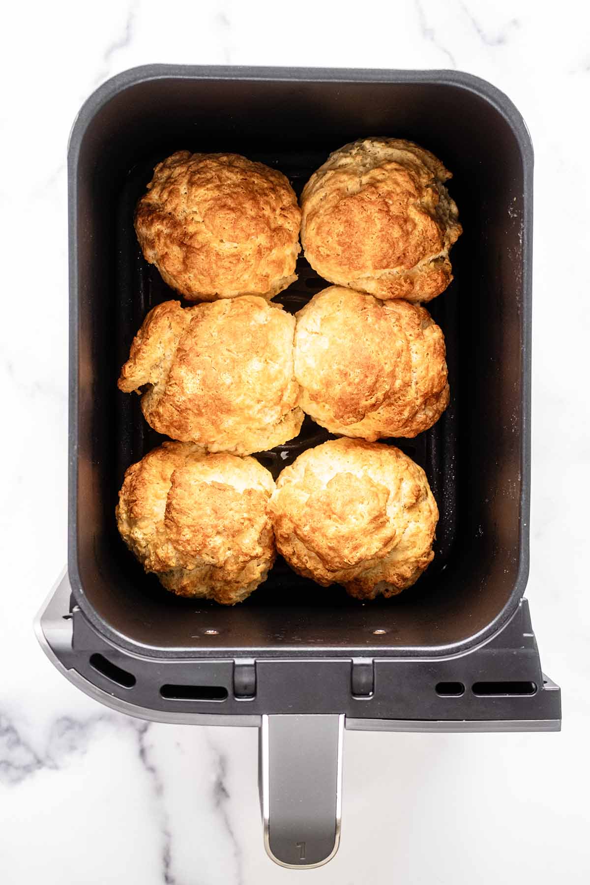 Six baked biscuits in an air fryer basket.