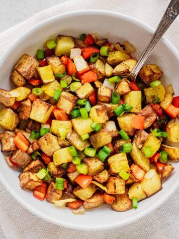 Overhead view of breakfast potatoes in a white bowl with a spoon on a white cloth napkin.