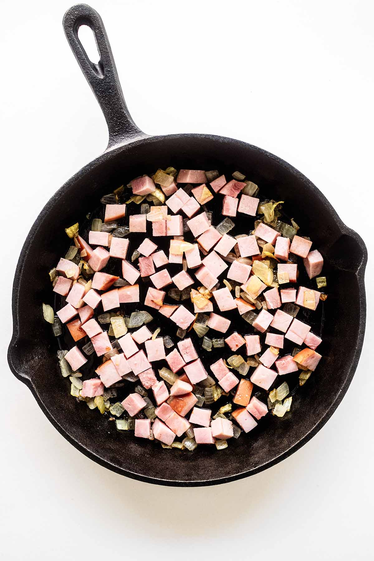 Overhead view of chopped onion and cubed ham in a cast iron skillet