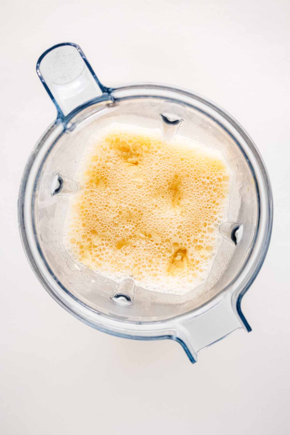 Overhead view of blended ingredients and grated Swiss cheese in a blender.