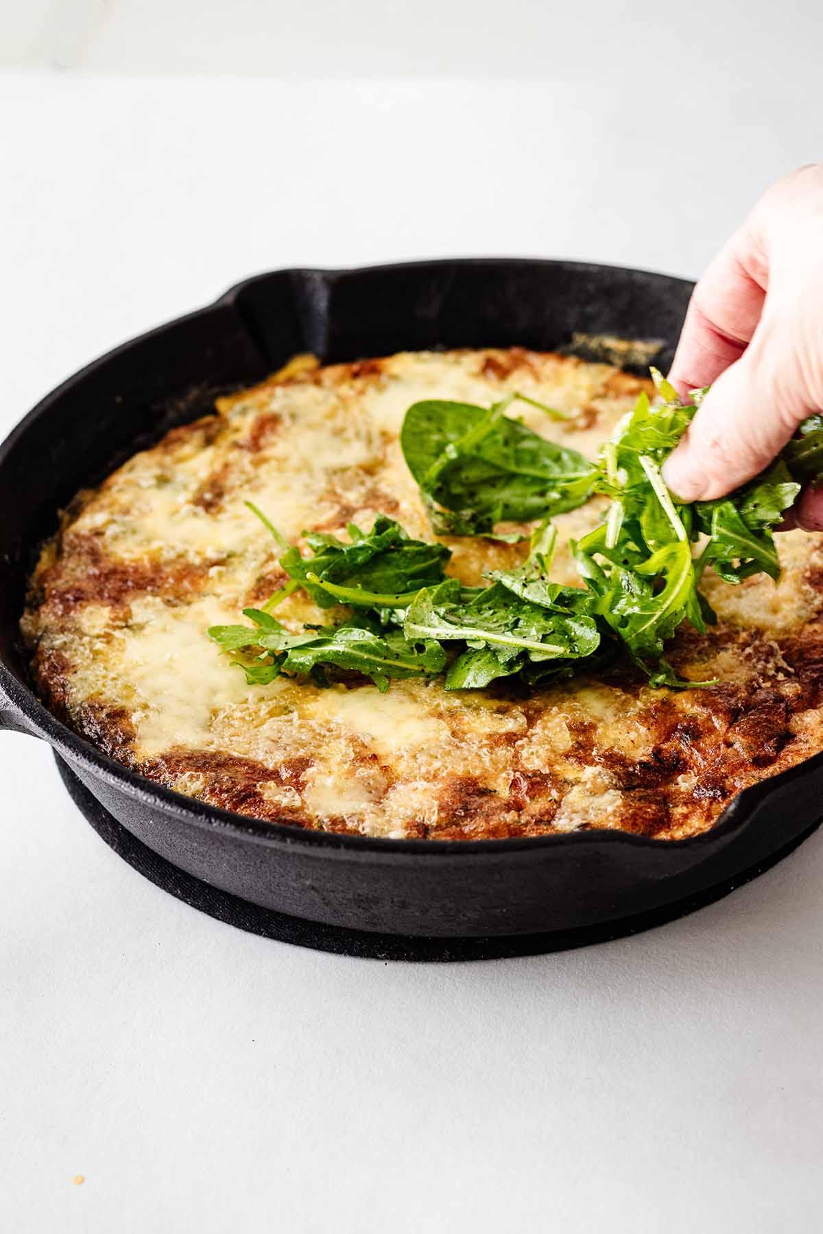 Front view of arugula being placed on top of frittata.