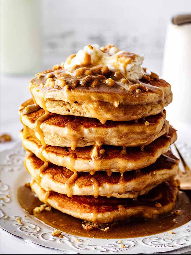 Stack of peanut butter pancakes topped with whipped cream on a white plate.