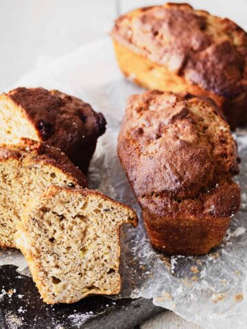 Slices and two loaves of air fryer banana bread on a dark cutting board