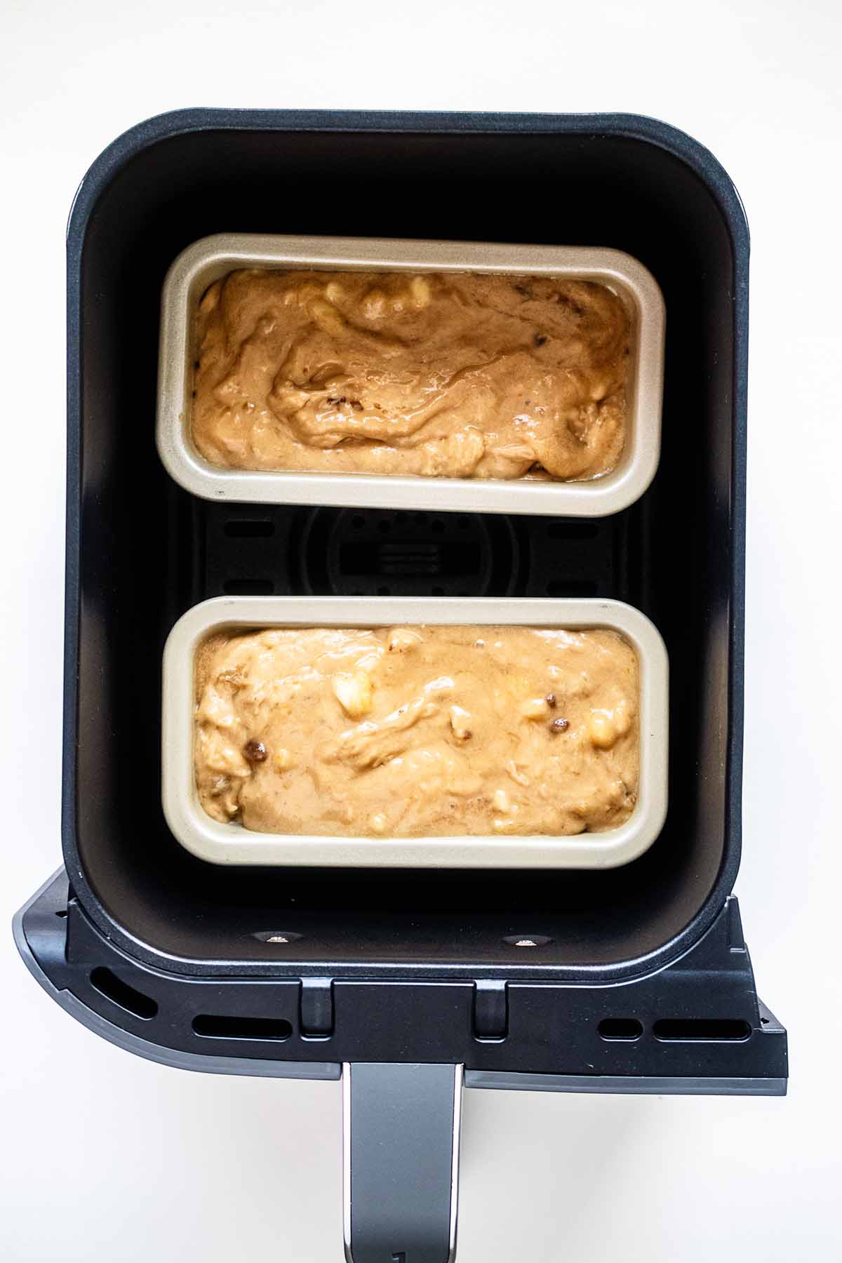 Mini loaf pans filled with banana bread batter in an air fryer basket.