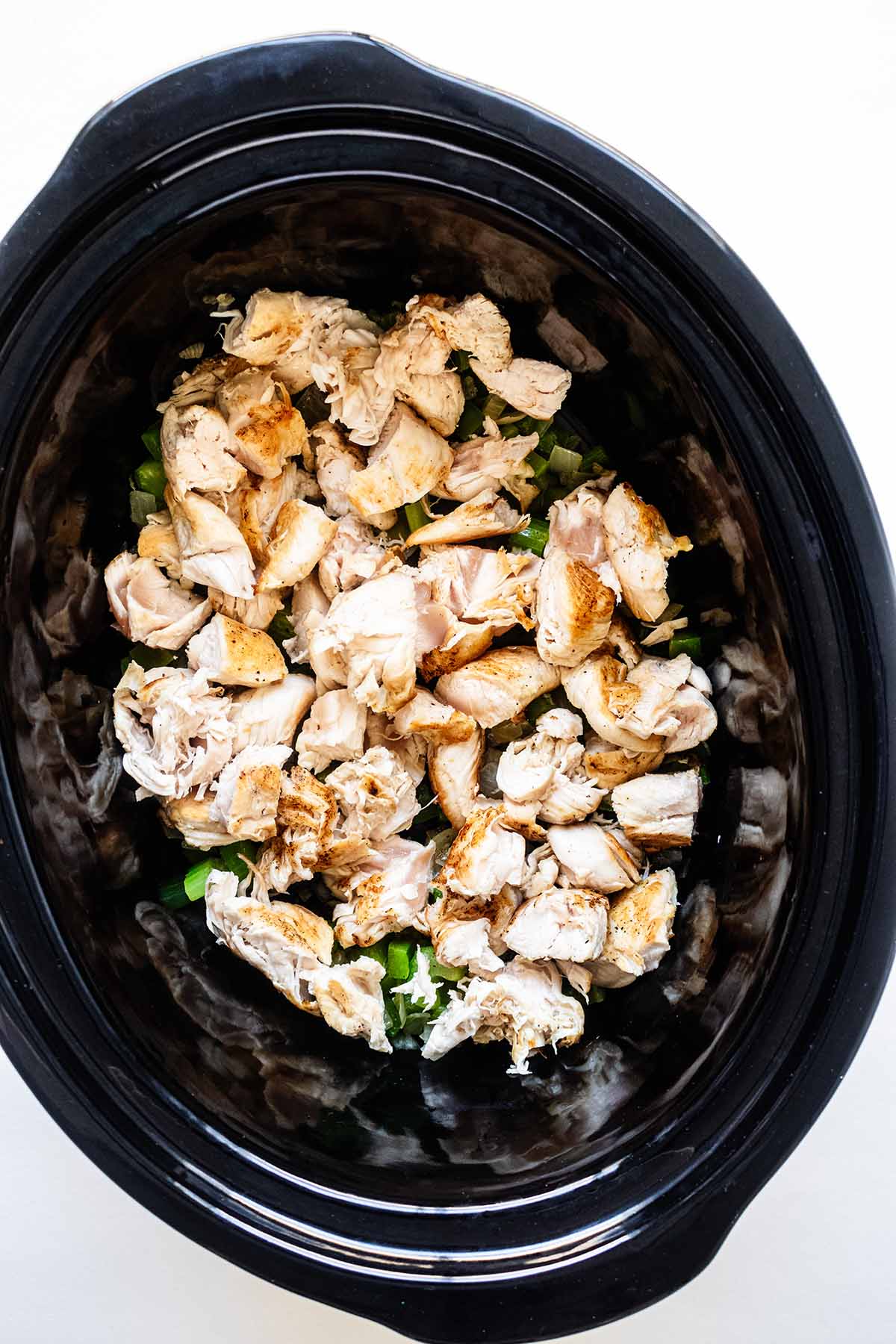 Seared chicken and cooked onion and celery in a slow cooker.