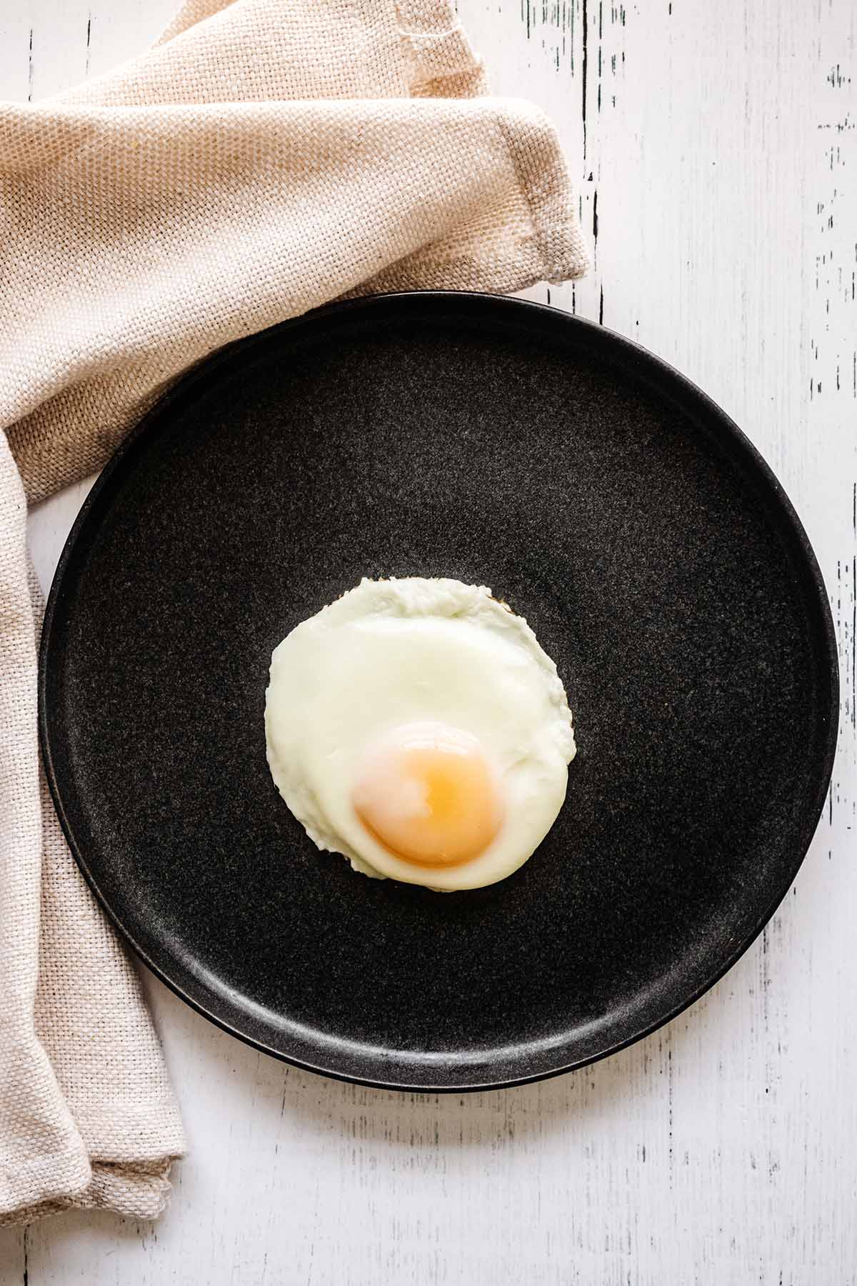 Basted egg on a dark grey plate with a beige napkin.