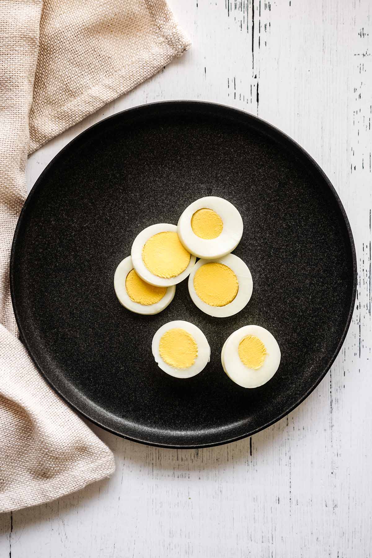 Sliced hard cooked egg on a dark grey plate with a beige napkin.