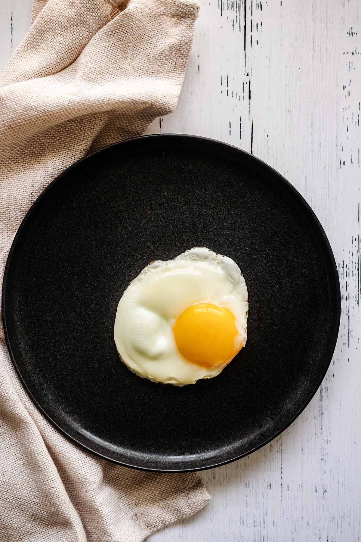 Sunny side up egg on a dark grey plate with a beige napkin.