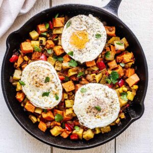 Sweet potato breakfast hash topped with three fried eggs in a cast iron skillet.