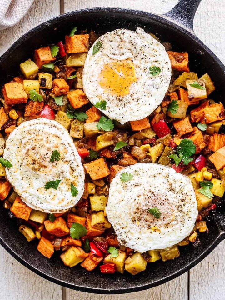 Sweet potato breakfast hash topped with three fried eggs in a cast iron skillet.