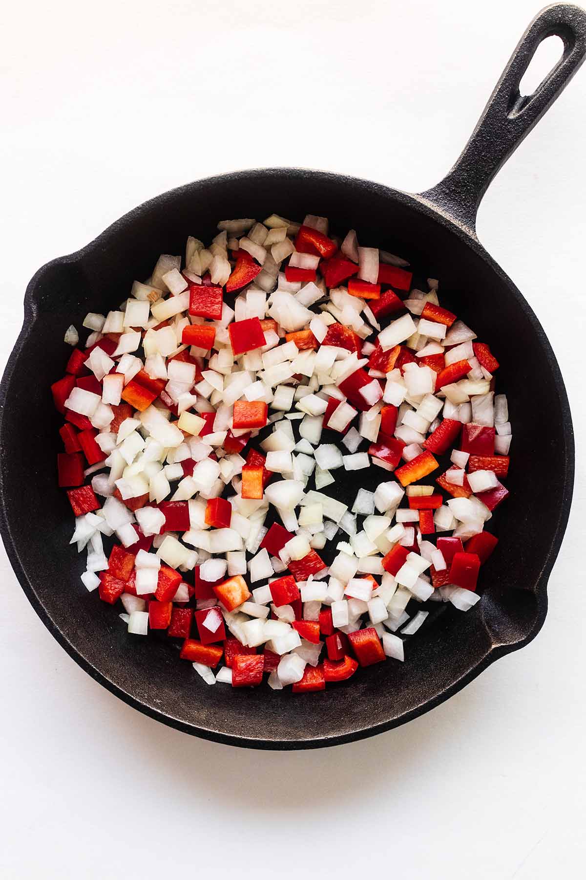 Chopped onion and red bell pepper in a cast iron skillet.