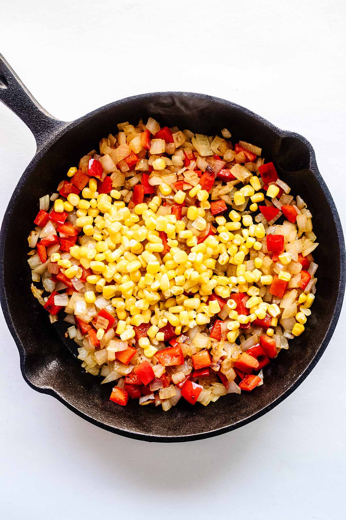 Chopped onion, red bell pepper and corn in a cast iron skillet.