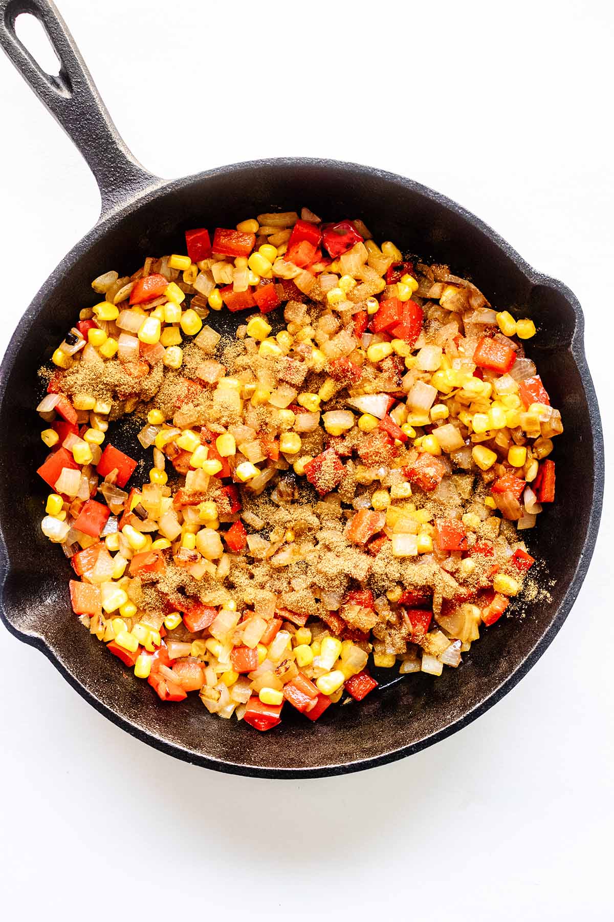 Cooked chopped onion, red bell pepper, corn, and ground cumin in a cast iron skillet.