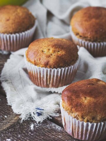 Five banana protein muffins on a white napkin on a dark wood table.