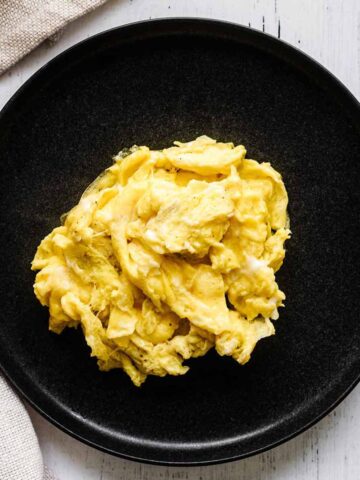 Scrambled eggs on a dark grey plate with a beige napkin.