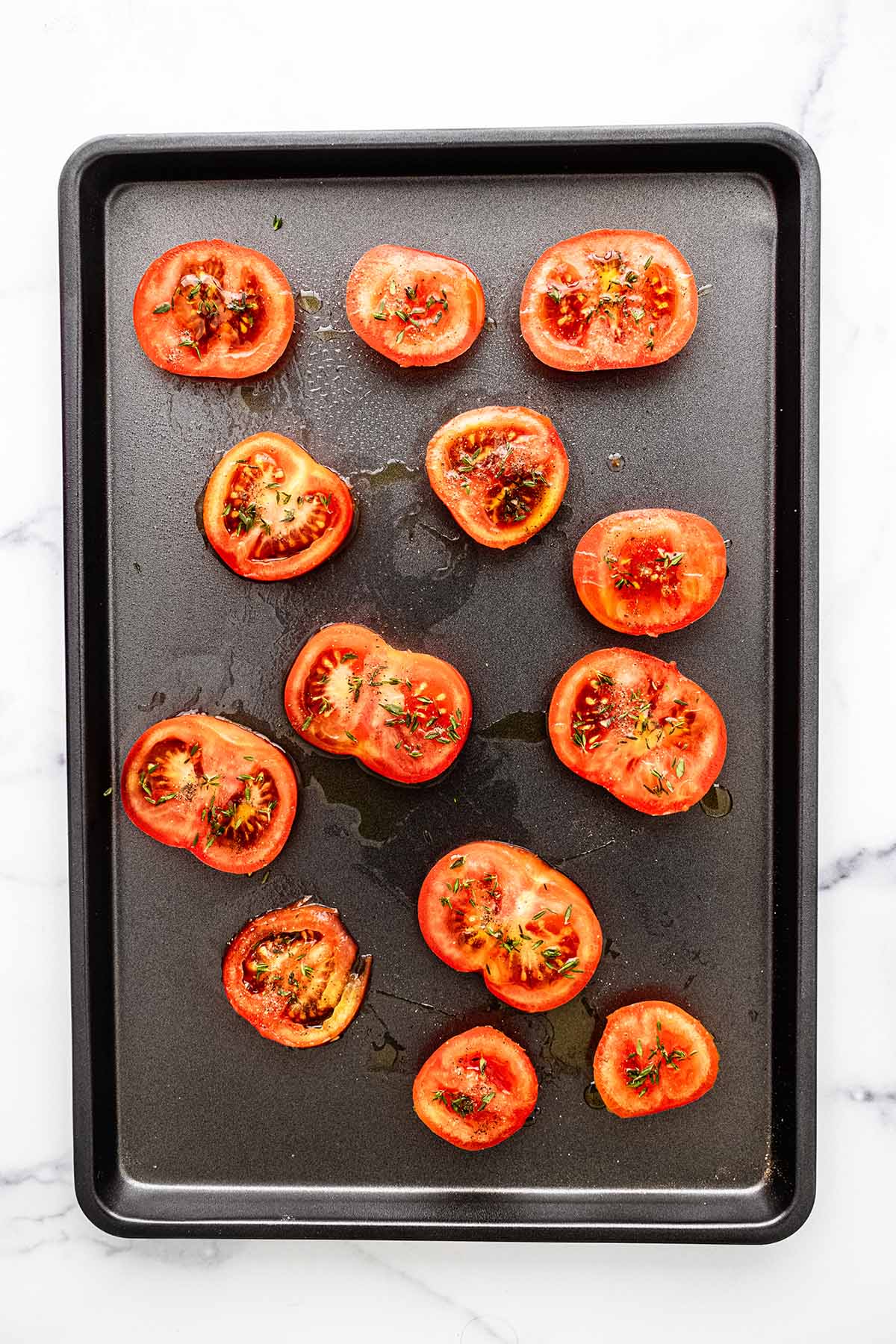 Tomato slices spread out on a baking sheet.