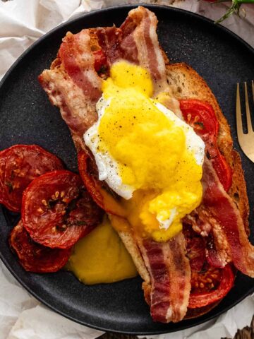 Eggs Blackstone on a dark grey plate with a gold fork.