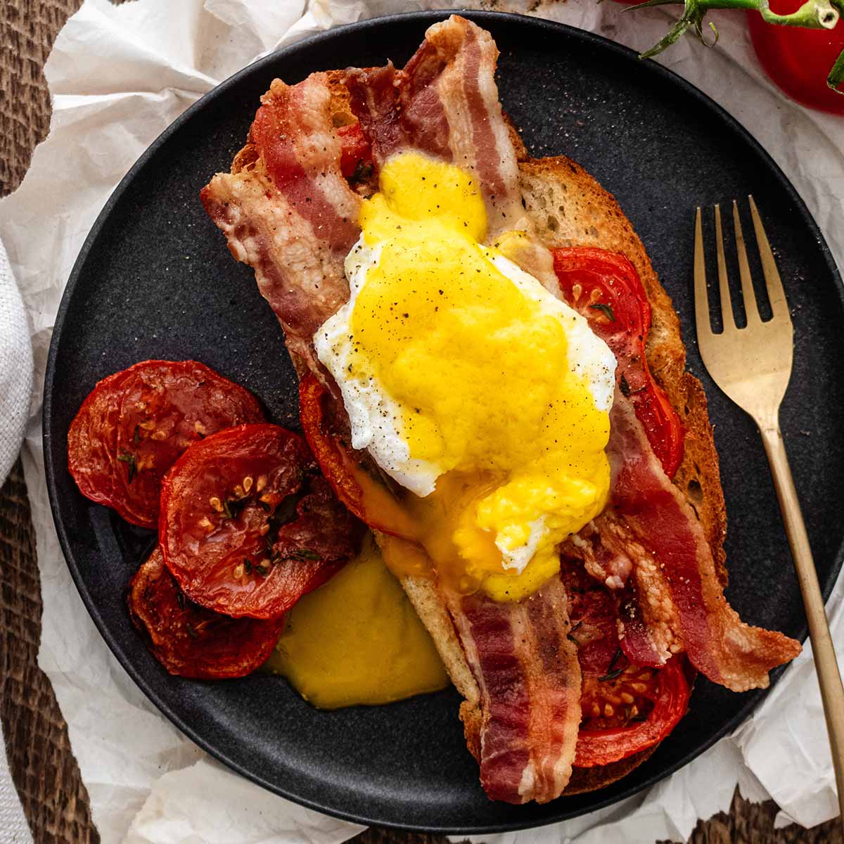 Eggs Blackstone on a dark grey plate with a gold fork.