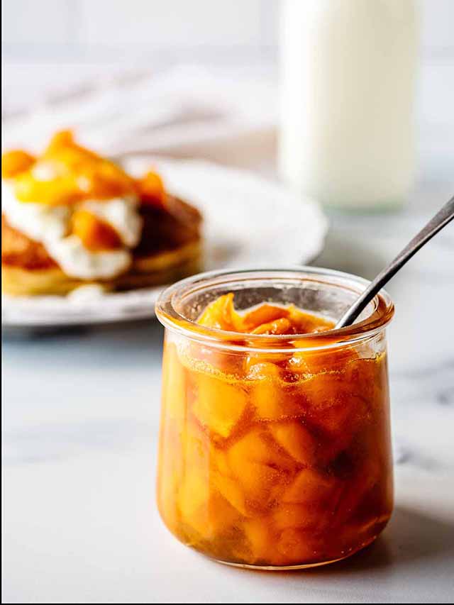 Mango compote in a small jar with a spoon.