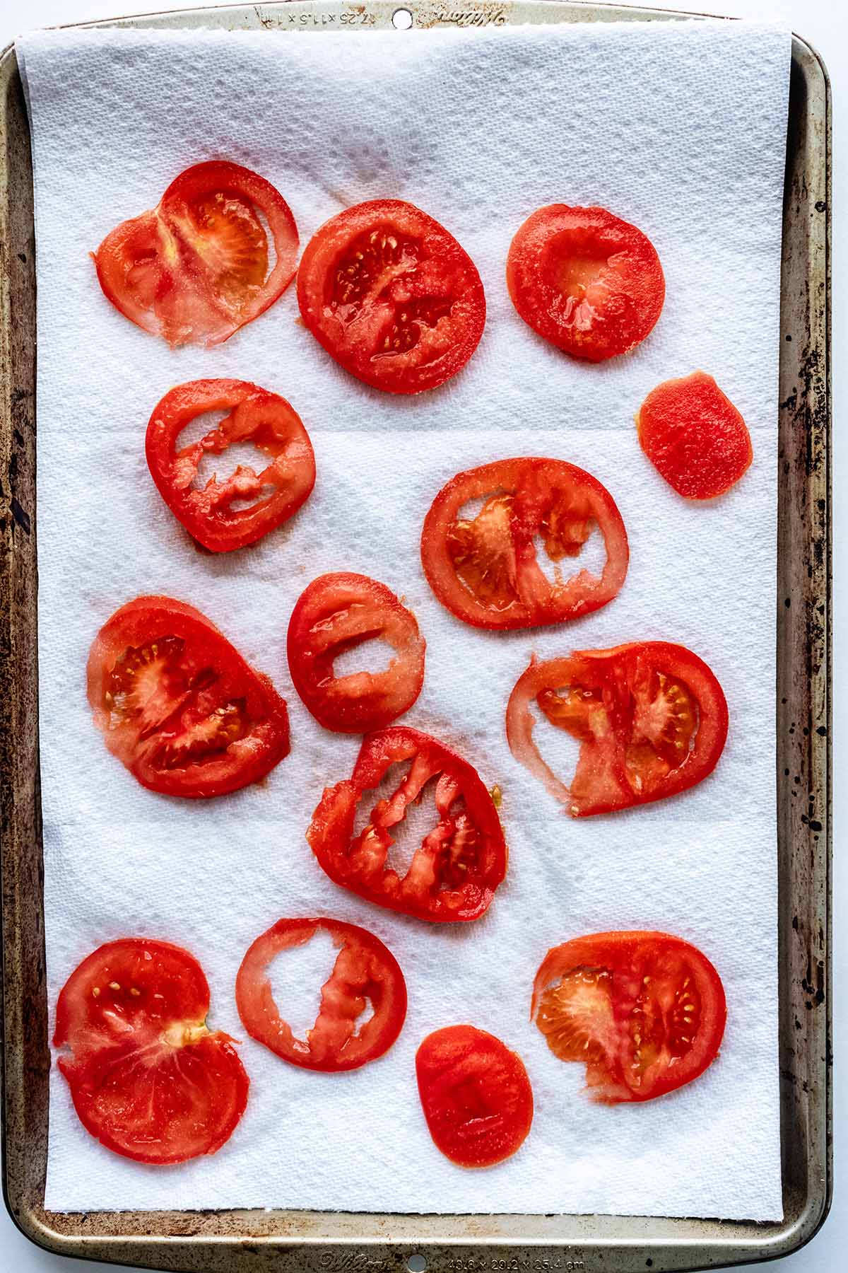 Sliced tomato on a paper towel in a baking sheet.