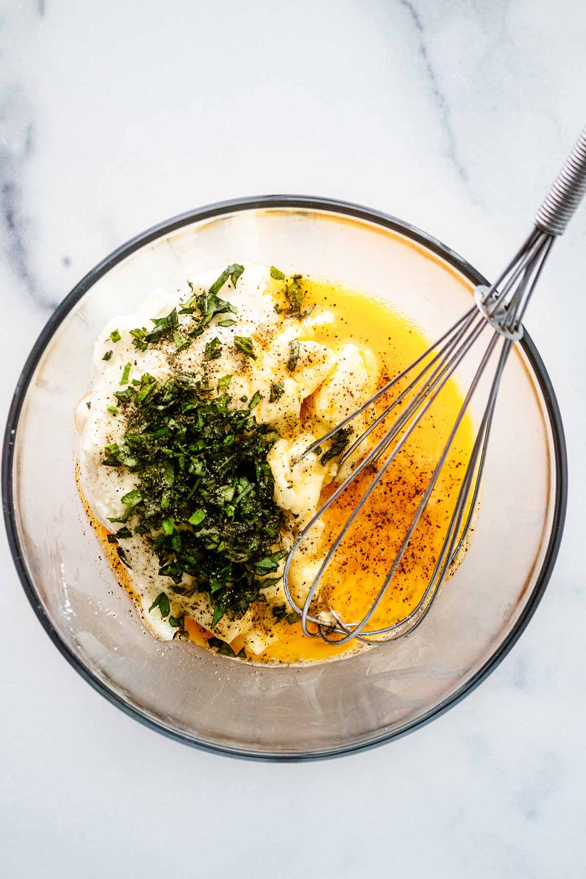 Ricotta cheese, egg, basil, salt and pepper in a glass bowl with a whisk.