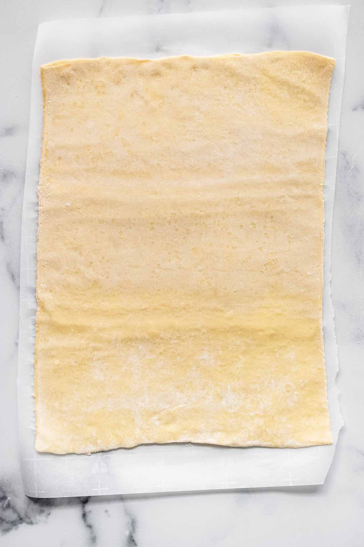 Puff pastry sheet on parchment paper on a marble countertop.